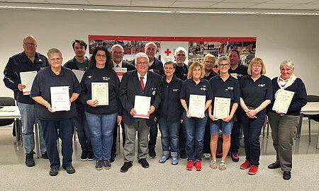 15 Personen stehen mit Ihren Urkunden in einer zweierreihe in einem beleuchteten Raum beim DRK Soest.